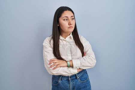 Téléchargez les photos : Jeune femme latine debout sur fond bleu regardant sur le côté avec les bras croisés convaincus et confiants - en image libre de droit