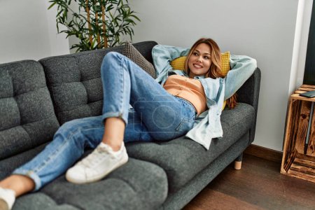 Téléchargez les photos : Jeune femme caucasienne souriant confiant couché sur le canapé à la maison - en image libre de droit