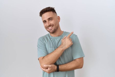 Photo for Hispanic man with beard standing over white background with a big smile on face, pointing with hand finger to the side looking at the camera. - Royalty Free Image