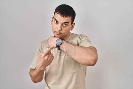 Téléchargez les photos : Jeune homme arabe portant t-shirt décontracté à la hâte pointant pour regarder le temps, l'impatience, regarder la caméra avec une expression détendue - en image libre de droit