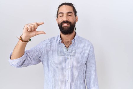 Téléchargez les photos : Homme hispanique avec barbe portant chemise décontractée geste souriant et confiant avec la main faisant signe de petite taille avec les doigts à la recherche et la caméra. concept de mesure. - en image libre de droit