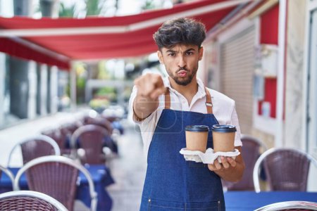 Photo for Arab man with beard wearing waiter apron at restaurant terrace pointing with finger to the camera and to you, confident gesture looking serious - Royalty Free Image