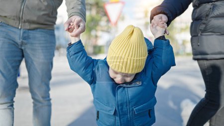 Téléchargez les photos : Blanc bambin souriant gai tenant la main avec maman et papa à la rue - en image libre de droit