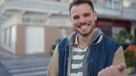 Foto de Joven caucásico hombre sonriendo confiado pidiendo a venir en la calle - Imagen libre de derechos