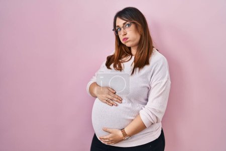 Photo for Pregnant woman standing over pink background puffing cheeks with funny face. mouth inflated with air, crazy expression. - Royalty Free Image