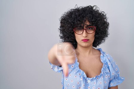 Photo for Young brunette woman with curly hair wearing glasses over isolated background looking unhappy and angry showing rejection and negative with thumbs down gesture. bad expression. - Royalty Free Image