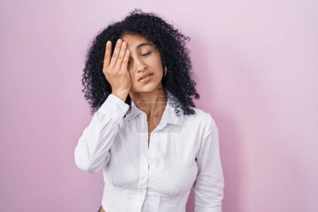 Photo for Hispanic woman with curly hair standing over pink background yawning tired covering half face, eye and mouth with hand. face hurts in pain. - Royalty Free Image
