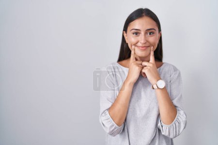 Photo for Young hispanic woman standing over white background smiling with open mouth, fingers pointing and forcing cheerful smile - Royalty Free Image