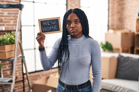 Foto de Mujer afroamericana sosteniendo pizarra con nueva actitud de pensamiento de texto en casa y expresión sobria buscando confianza en sí misma - Imagen libre de derechos