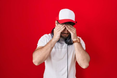 Photo for Hispanic man with beard wearing gamer hat and headphones suffering from headache desperate and stressed because pain and migraine. hands on head. - Royalty Free Image
