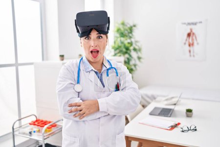 Photo for Young hispanic doctor woman wearing doctor uniform and virtual reality glasses afraid and shocked with surprise and amazed expression, fear and excited face. - Royalty Free Image