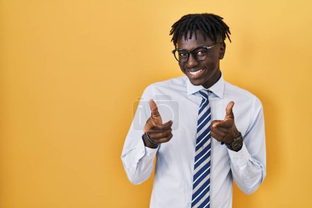Foto de Hombre africano con rastas de pie sobre fondo amarillo señalando los dedos a la cámara con la cara feliz y divertida. buena energía y vibraciones. - Imagen libre de derechos