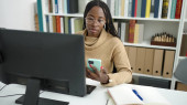 African woman using computer taking notes with smartphone at library university Poster #648218274