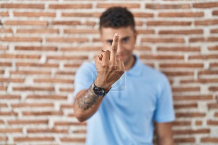 Téléchargez les photos : Brazilian young man standing over brick wall showing middle finger, impolite and rude fuck off expression - en image libre de droit