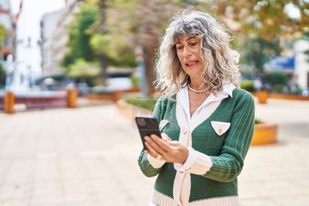 Téléchargez les photos : Middle age woman smiling confident using smartphone at park - en image libre de droit