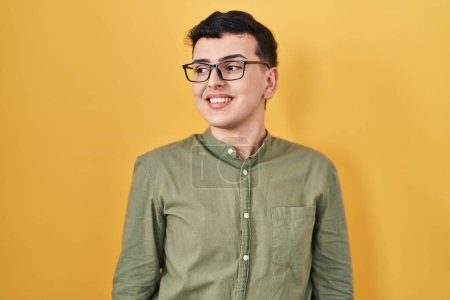 Photo for Non binary person standing over yellow background looking away to side with smile on face, natural expression. laughing confident. - Royalty Free Image
