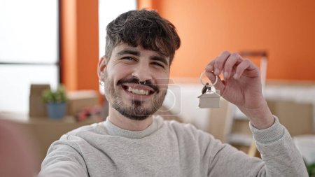Photo for Young hispanic man smiling holding new house keys taking selfie at new home - Royalty Free Image