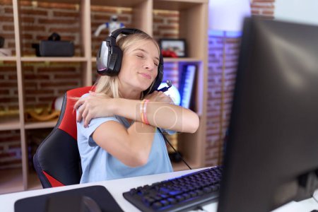 Foto de Joven mujer caucásica jugando videojuegos con auriculares abrazándose feliz y positivo, sonriendo confiado. amor propio y cuidado personal - Imagen libre de derechos