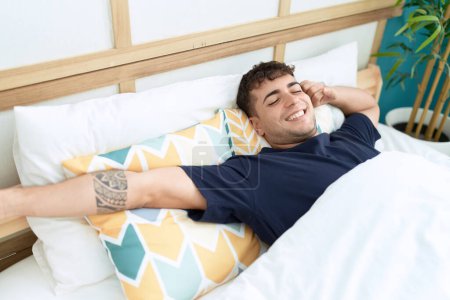 Téléchargez les photos : Young hispanic man waking up stretching arms at bedroom - en image libre de droit