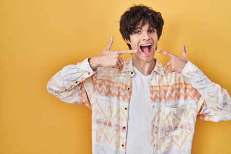 Téléchargez les photos : Jeune homme portant une chemise d'été décontractée souriant joyeuse montrant et pointant du doigt les dents et la bouche. concept de santé dentaire. - en image libre de droit