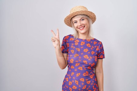 Téléchargez les photos : Jeune femme caucasienne portant des fleurs robe et chapeau d'été montrant et pointant vers le haut avec les doigts numéro deux tout en souriant confiant et heureux. - en image libre de droit