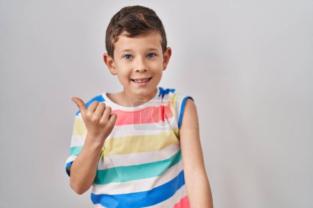 Foto de Joven niño caucásico recibiendo la vacuna mostrando el brazo con la tirita apuntando el pulgar hacia el lado sonriendo feliz con la boca abierta - Imagen libre de derechos