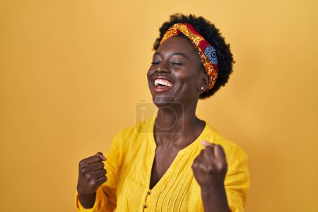 Photo for African young woman wearing african turban very happy and excited doing winner gesture with arms raised, smiling and screaming for success. celebration concept. - Royalty Free Image