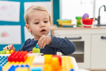 Téléchargez les photos : Adorable bambin blond jouant avec des blocs de construction assis sur la table à la maternelle - en image libre de droit