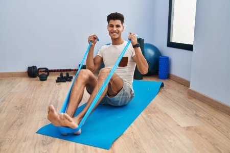 Photo for Young hispanic man smiling confident training using elastic band at sport center - Royalty Free Image