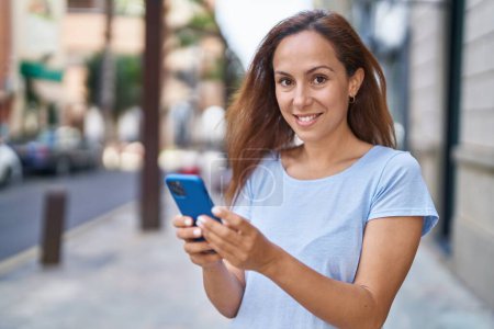 Téléchargez les photos : Jeune femme souriant confiant en utilisant smartphone à la rue - en image libre de droit