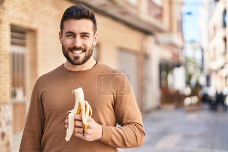 Photo for Young hispanic man smiling confident eating banana at street - Royalty Free Image