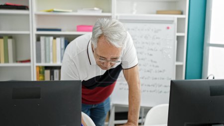 Foto de Hombre de mediana edad con profesor universitario de pelo gris usando computadora en el aula universitaria - Imagen libre de derechos