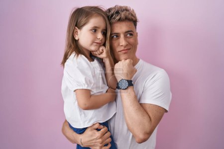 Photo for Young father hugging daughter over pink background serious face thinking about question with hand on chin, thoughtful about confusing idea - Royalty Free Image