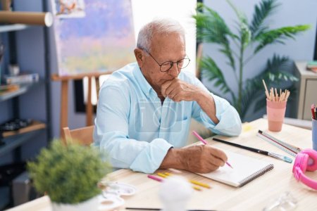 Téléchargez les photos : Senior grey-haired man artist drawing on notebook with doubt expression at art studio - en image libre de droit
