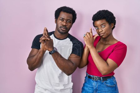 Photo for Young african american couple standing over pink background holding symbolic gun with hand gesture, playing killing shooting weapons, angry face - Royalty Free Image