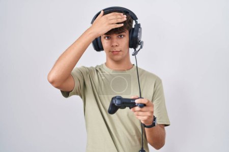 Téléchargez les photos : Adolescent hispanique jouant contrôleur de tenue de jeu vidéo surpris avec la main sur la tête pour erreur, rappelez-vous erreur. oublié, mauvais concept de mémoire. - en image libre de droit