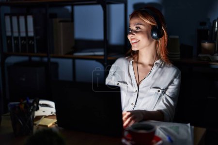 Photo for Young caucasian woman working at the office at night looking away to side with smile on face, natural expression. laughing confident. - Royalty Free Image