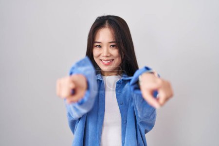 Foto de Joven mujer china de pie sobre fondo blanco señalando a usted y la cámara con los dedos, sonriendo positiva y alegre - Imagen libre de derechos
