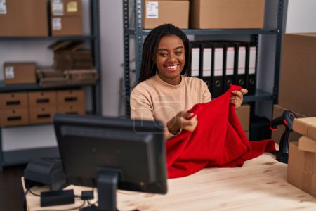 Téléchargez les photos : Africaine américaine femme commerce électronique travailleur d'affaires tenant pull au bureau - en image libre de droit