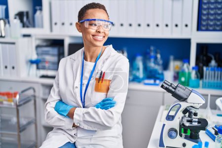 Photo for African american woman scientist smiling confident sitting with arms crossed gesture at laboratory - Royalty Free Image