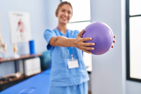 Photo for Young hispanic woman physiotherapist stretching arms using ball at rehab clinic - Royalty Free Image