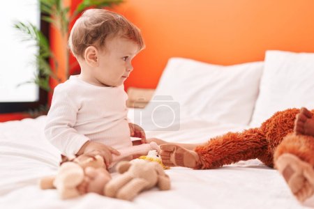 Photo for Adorable blond toddler holding doll sitting on bed at bedroom - Royalty Free Image