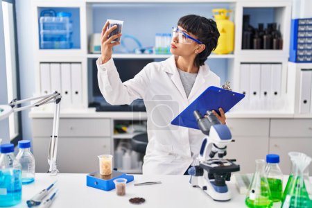 Photo for Young woman scientist holding clipboard and sample at laboratory - Royalty Free Image
