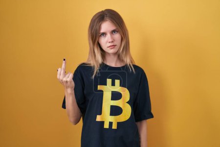 Téléchargez les photos : Blonde caucasian woman wearing bitcoin t shirt showing middle finger, impolite and rude fuck off expression - en image libre de droit