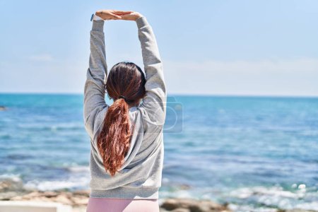 Photo for Young hispanic woman stretching arms standing on back view at seaside - Royalty Free Image