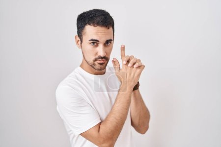 Photo for Handsome hispanic man standing over white background holding symbolic gun with hand gesture, playing killing shooting weapons, angry face - Royalty Free Image