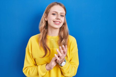 Téléchargez les photos : Jeune femme caucasienne debout sur fond bleu applaudissant heureux et joyeux, souriant mains fières ensemble - en image libre de droit