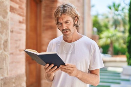 Photo for Young blond man smiling confident reading book at street - Royalty Free Image