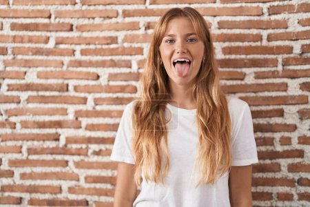 Téléchargez les photos : Jeune femme caucasienne debout sur le mur de briques langue collante heureux avec une expression drôle. concept d'émotion. - en image libre de droit