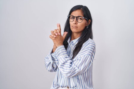 Téléchargez les photos : Jeune femme hispanique portant des lunettes tenant une arme symbolique avec geste de la main, jouant tuer des armes de tir, visage en colère - en image libre de droit